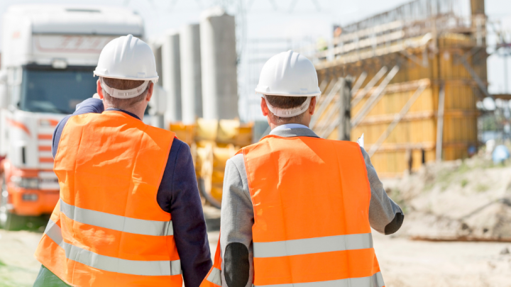 Two people in hard hats and safety vests stand at a construction site with a telematics-equipped truck, showing connected jobsite.