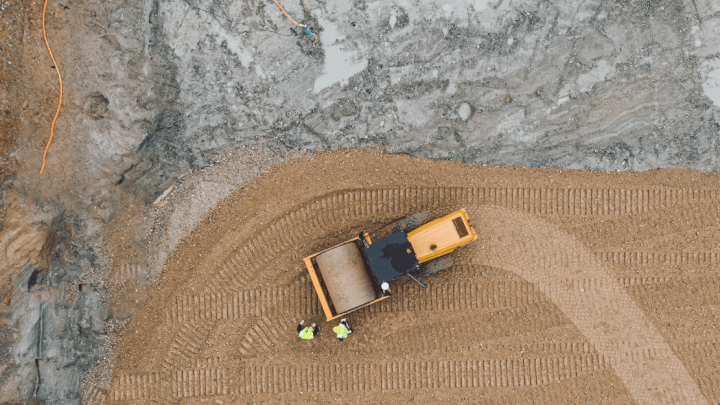 Aerial view of a construction site with a yellow bulldozer using Trackunit tech, workers nearby, and tire tracks—construction IoT.