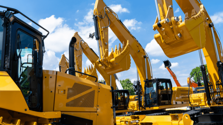 Large yellow excavators with telematics are lined up outdoors under a blue sky, their arms raised against trees in the background.