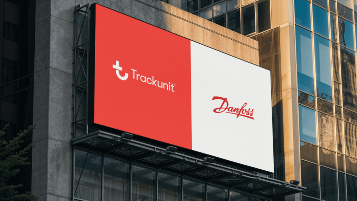 A large billboard on a city building displays the Trackunit logo on red next to Danfoss on white, framed by glass windows.