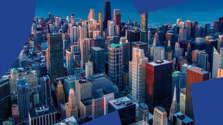 Aerial cityscape at sunset with tall skyscrapers, blue geometric borders, and water—an inspiring view for connected jobsite innovation.