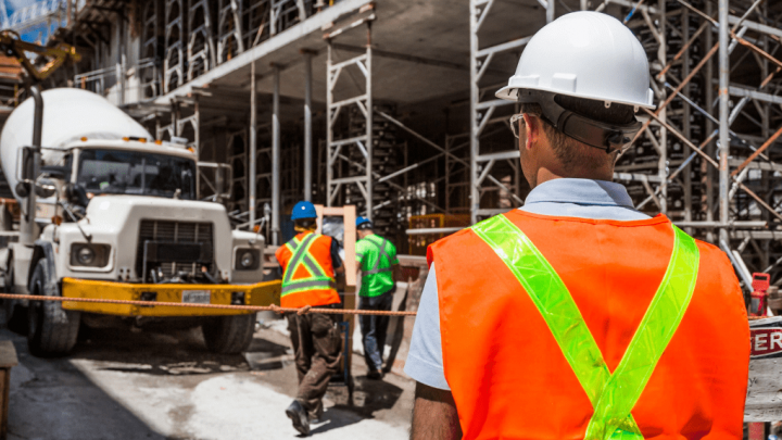 A worker in a hard hat and safety vest oversees a cement truck at an eco-friendly construction site, highlighting connected jobsite.