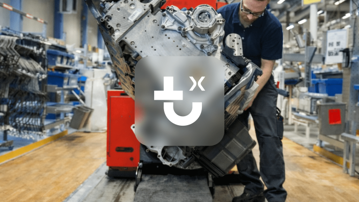 A worker uses a red IrisX machine to move an engine block in a factory, highlighting construction IoT on the busy shop floor.